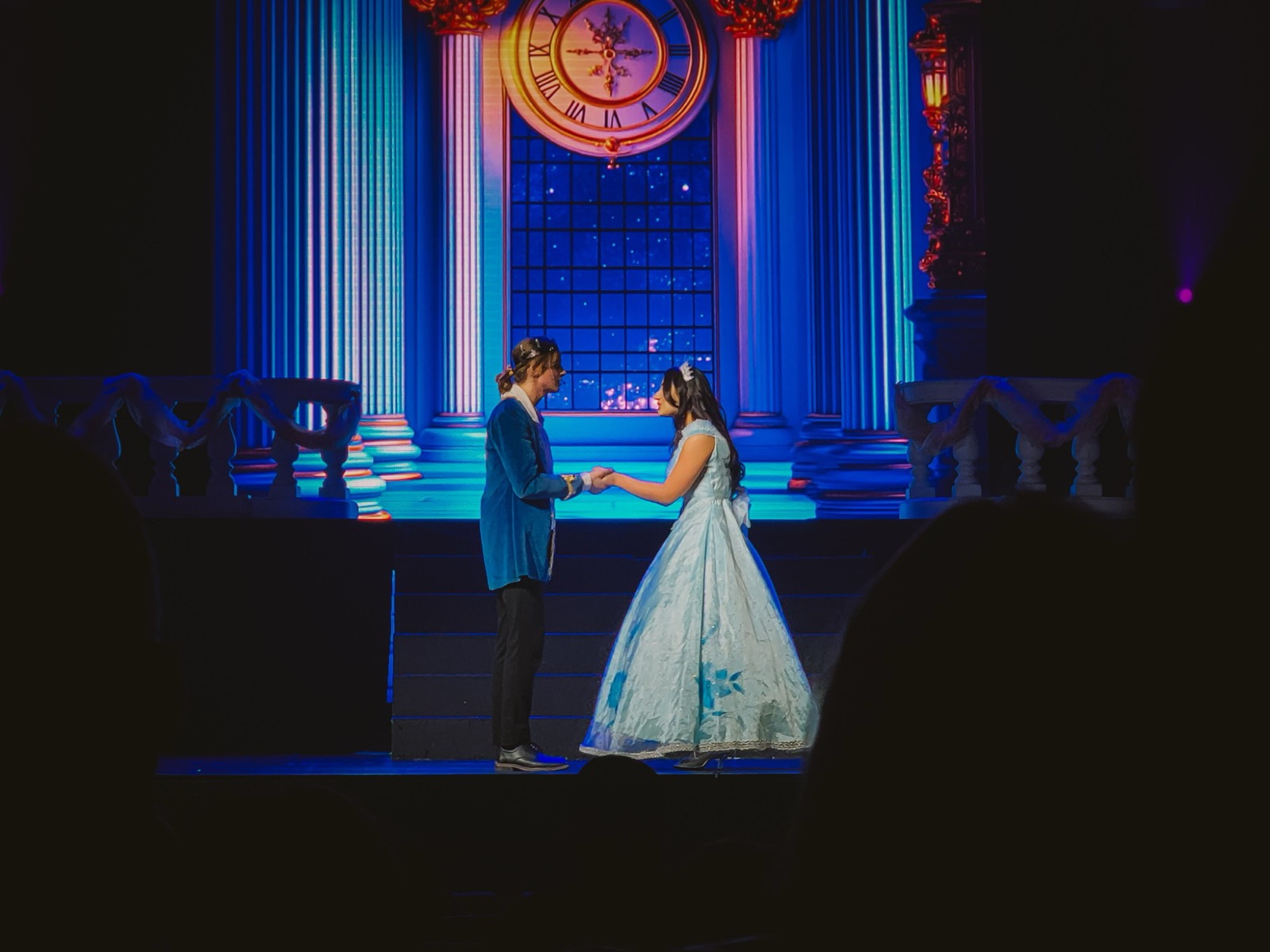 Two student leads in Cinderella under blue light, in front of a projected palace clock
