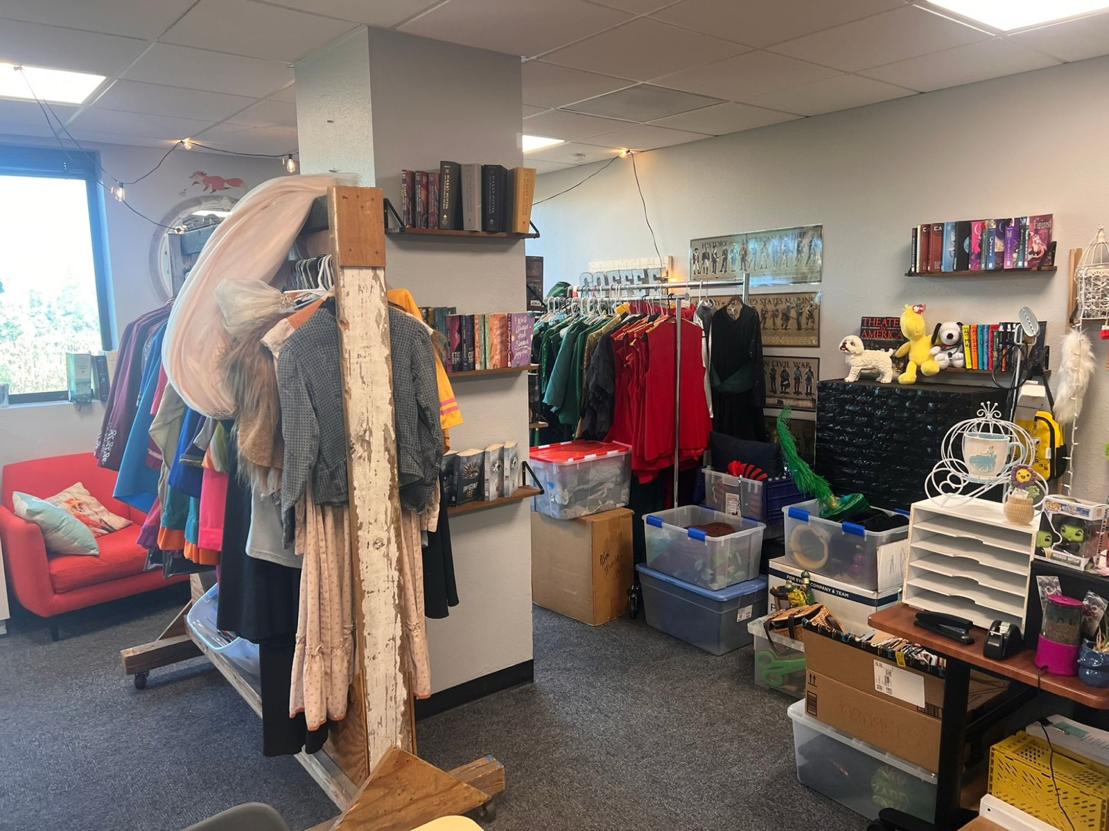 A classroom corner filled with costume racks, prop bins, and theater books