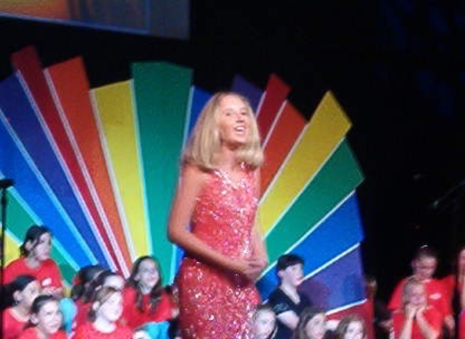 A young Taylor Fox performing in a red sequin dress in front of a rainbow set